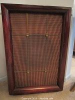 Front view of the speaker showing wooden framed woven fabric grill.