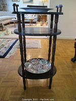 Straight front view of the dark wood three-tier side table showing the middle and bottom shelves with ceramic plates.