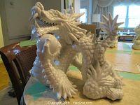 Front and side views of the glossy white ceramic dragon figurine showing detailed scales, spikes, claws, and open mouth.