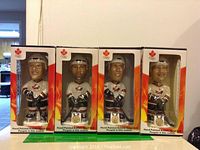 Four hand painted hockey bobble heads in original boxes showing front view of each player including helmets, white jerseys with Team Canada logo, black hockey pants, and sticks.