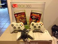 Xbox 360 controllers and game cases in front of Xbox retail box.
