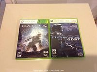 Two Xbox 360 shooter game cases: Halo 4 and Halo 3 ODST on a beige table.