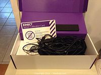 Xbox 360 Kinect sensor calibration card and cables inside a white and purple box.