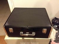 Closed black hard shell case with silver metal clasp and handle, with corner reinforcements