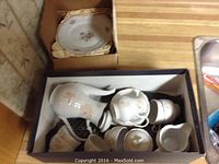 A box containing the teapot, cups, sugar bowl with lid, and creamers showing floral china pieces.