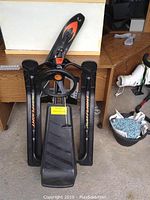Front view of black child's sled with steering wheel and footrest, showing decal details and plastic skis.