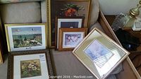 Several framed prints arranged on a couch and table, showing a variety of floral and landscape artworks.