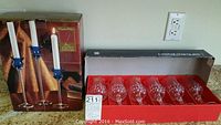 Photo showing boxed set of six Cristal d'Arques crystal goblets in red box and boxed set of three cobalt glass candlestick holders with white candles.
