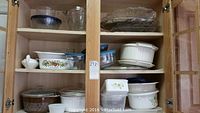 Two wooden cabinets with clear glass doors containing various cookware and casserole dishes including Pyrex and Rubbermaid items. Items are arranged on four shelves including glass bowls, ceramic casseroles, plastic containers, and lids.