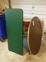 Photo of oval brown wooden card table and rectangular green card table folded and stacked vertically.