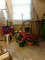 Overview of various gardening supplies including rakes, buckets, baskets and garden cart near a window.