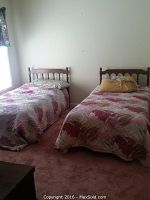 Two twin beds in a room with patterned bedding, showing the bed on the left side for sale.