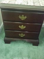 Close-up photo showing the front of one three-drawer side table with dark wood finish and brass drawer pulls.
