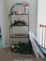 Full view of black metal shelving unit with decorative items including vase with faux flowers, candles, greenery, decorative box, and glass dish