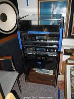 Fisher stereo components stacked in black cabinet rack with glass door, featuring blue protective tape on sides.