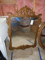 Full view of antique gold-framed mirror showing the entire rectangular shape with detailed elaborate carvings on the frame and aged mirror glass.
