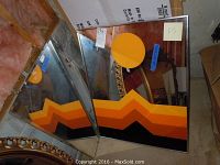 Photo of two decorative framed mirrors with orange geometric designs and silver frames, showing the full mirrors and partial background.
