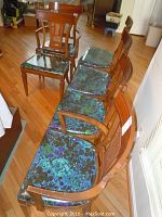 Six wooden dining chairs arranged in a row with cane backs and blue-green floral fabric seats protected by plastic. Chairs sit on hardwood flooring.