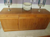 Front view of teak wood buffet showing three top drawers and three cabinet doors with recessed and vertical handles respectively, placed on carpeted floor.