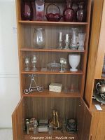 Shelving unit with ruby glass vases, clear glass vases, candle holders, picture frames, milk bottles, and other decor items.