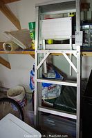 Folded 5-foot aluminum step ladder leaning against a shelf with miscellaneous items around it in a garage.