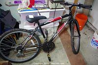 Full view of a black and red Roadmaster Mt Fury 5 speed mountain bike against a storage background.