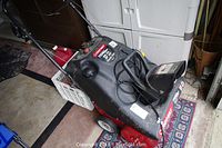 View from top corner showing gas tank, power cord, and handlebar controls of the black and red Troy-Bilt snow thrower.