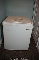 Front view of the closed white Magic Chef mini refrigerator with manual on top.