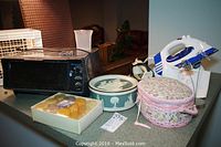 Group photo of multiple household items including sewing kits, irons, toaster oven, and candles on countertop.