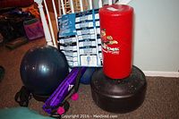 Photo of red Kid Kick heavy bag with cartoon branding on black base alongside exercise balls and purple mat.