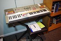 Full view of Casio LK-94TV keyboard on X-style stand with padded stool underneath, manuals placed on stool.