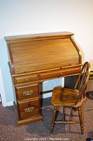 Full view of the wood roll top desk with child's chair, roll top closed.