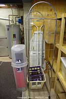 Photo of a metal laundry rack with baskets, a tall translucent pink bin, and white plastic laundry baskets in a basement storage area.
