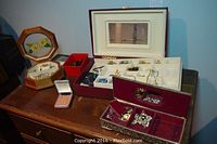 Multiple jewelry boxes on wooden surface containing assorted costume jewelry pieces