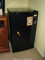 Black mini refrigerator with closed door showing a paper and magnet