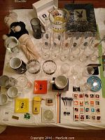 Full lot overview showing stuffed rabbit doll, large variety of Playboy branded drinking glasses, mugs, ashtrays, and matchbooks arranged on a flat surface.