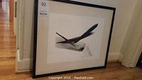 Full view of framed lithograph leaning against wall on hardwood floor