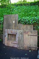 Full view of 4 old wooden barn doors leaning against a wall, showing overall size and wear
