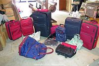 Photo showing all luggage including four red Stratus luggage pieces, two large black Travel Gear luggage pieces, smaller bags and cases arranged on floor.