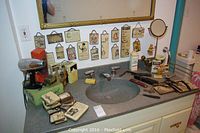 Overall view of countertop showing razors, brushes, mirror, hair dryer, bottles, boxes and wood plaques