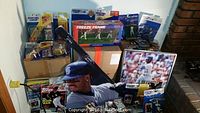 Various Ken Griffey Jr and Frank Thomas baseball cards and collectibles displayed against a wall and on a table, featuring Starting Lineup figures, Freeze Frame set, large Griffey cutout, and framed print with broken glass.