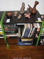 Full view of figurines arranged on top of a black table with books on shelves below.