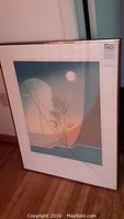 Framed print with broken glass showing an abstract composition with plant and moon.