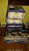 Stack of seven labeled reel-to-reel tape cartridges atop vinyl pile with a cassette on the side