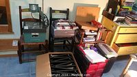 Wide view showing overhead projector, laminator on chair, Canon printer with ink cartridges, box of leather binders, paper cutter and shredder, along with miscellaneous office supplies and paper stacks