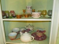 Full shelf view showing collection of multicolored brandy glasses, brown and beige bowls, Italian stamped vase, and cups