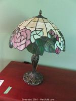 Full view of the table lamp showing metal base and stained glass style mosaic shade with pink rose and green leaves pattern.