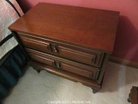 Pair of wood nightstands placed beside a bed, showing top, sides, and drawer fronts featuring metal pulls.