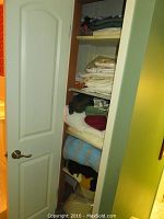 Closet shelf with folded crocheted afghans including a blue and tan chevron patterned afghan and black and tan afghan.