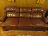 Front view of the brown leather sofa with cushioned back and seat and nailhead trim on arms.